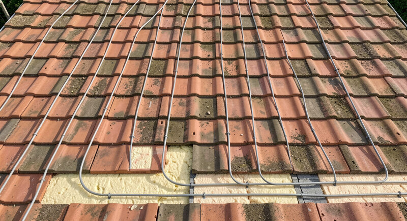 A tiled roof seen from above with thin pipe loops running between the tiles and the insulation.